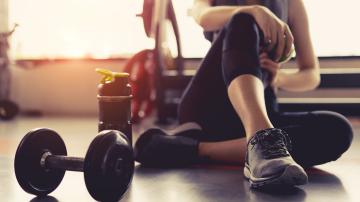 Woman sitting on gym floor next to water bottle and dumbell